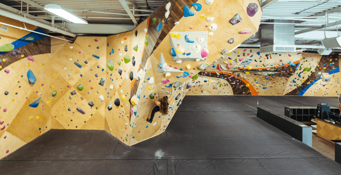 A woman climbing a steep indoor bouldering wall