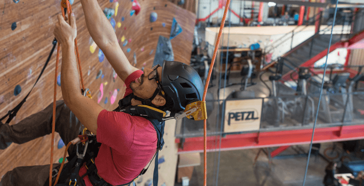 A route setter in Petzl safety gear ascending a climbing wall