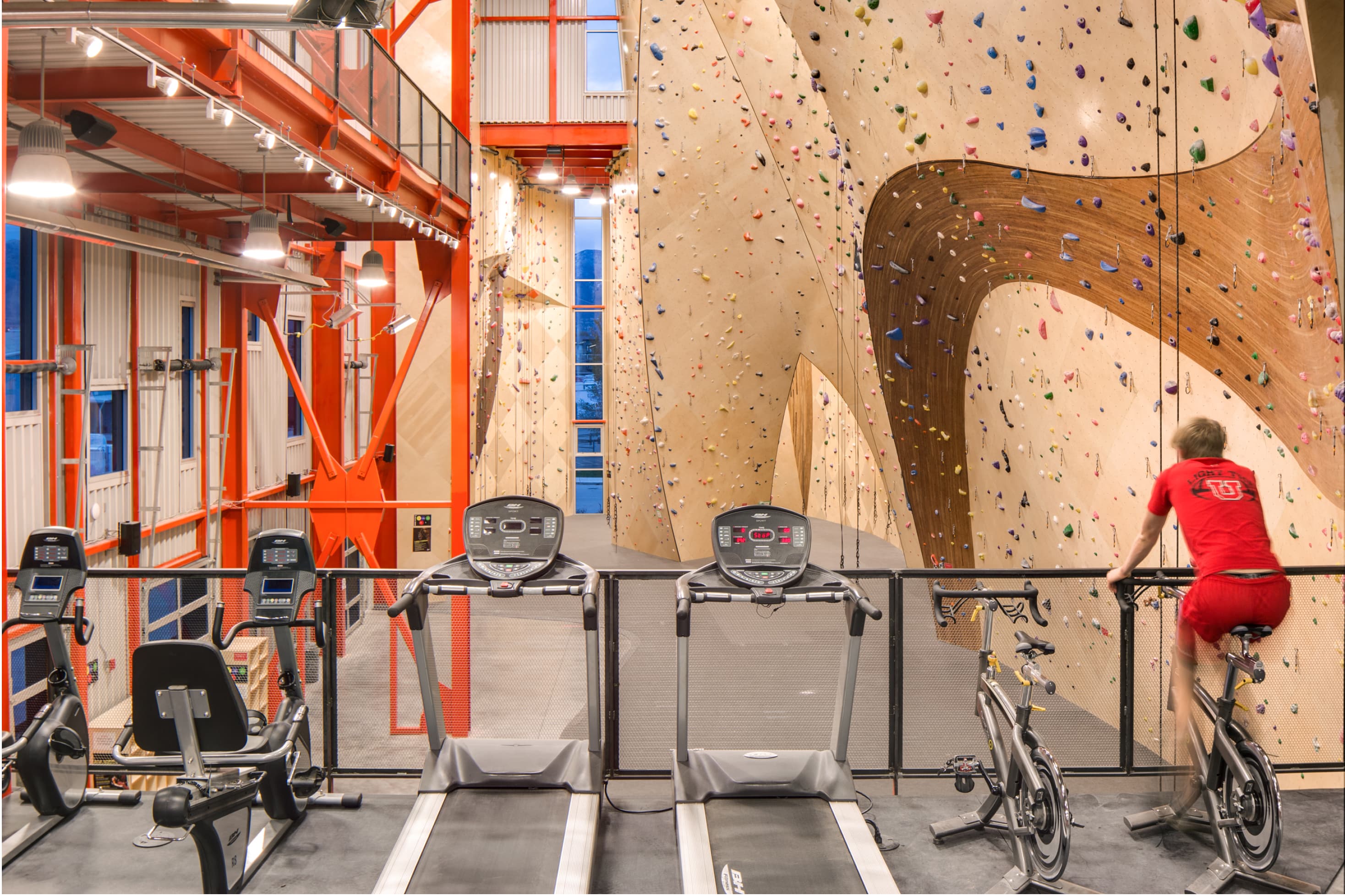 A man on a spin bike overlooks an indoor climbing gym