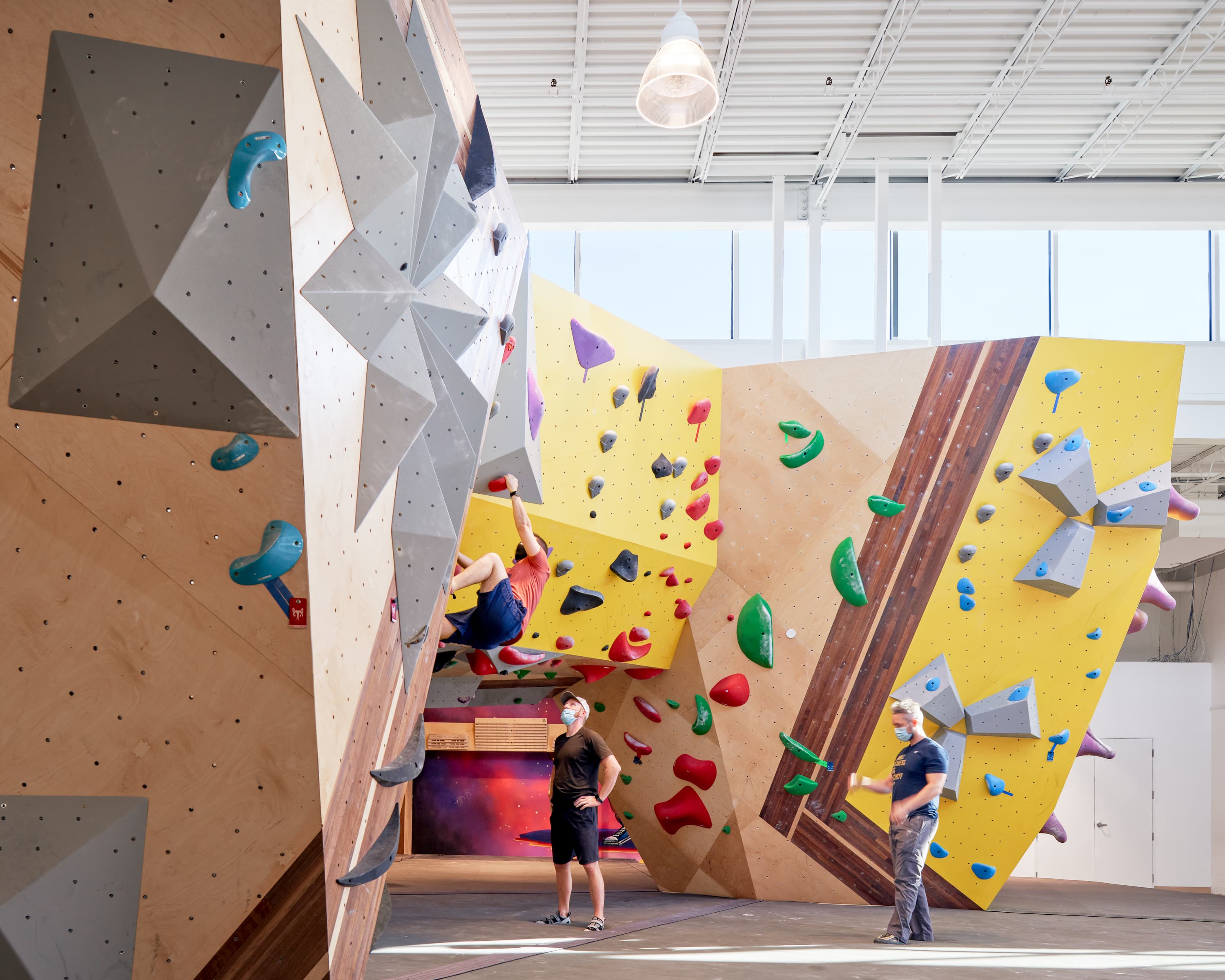 Climbers hanging on sunny, colorful SLM climbing walls custom built by Vertical Solutions