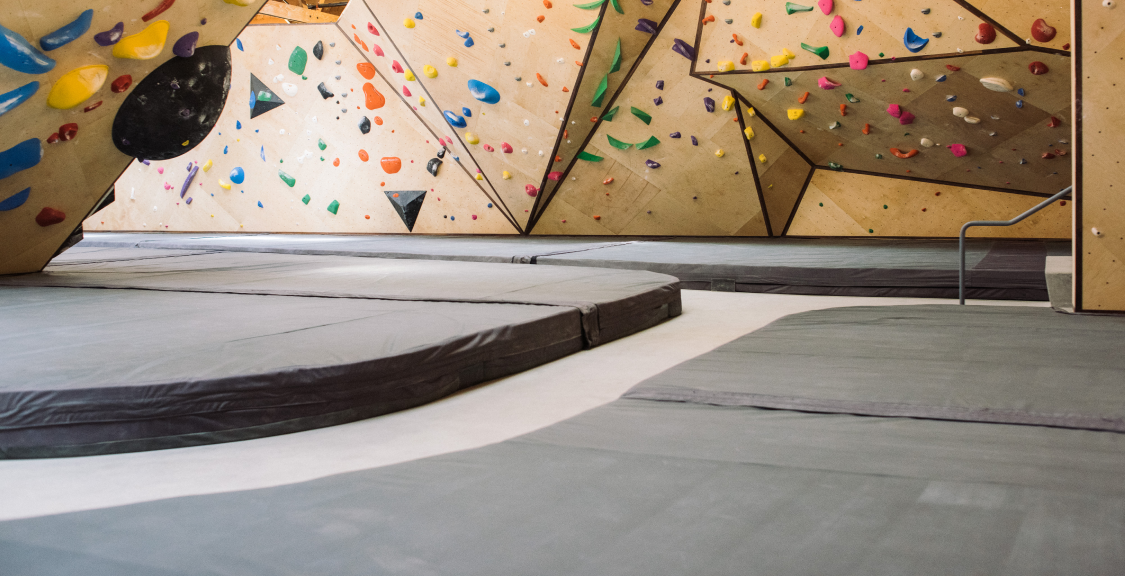 Curved bouldering pads in front of birch climbing walls