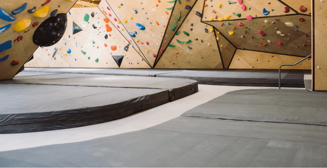 Curved bouldering pads in front of birch climbing walls