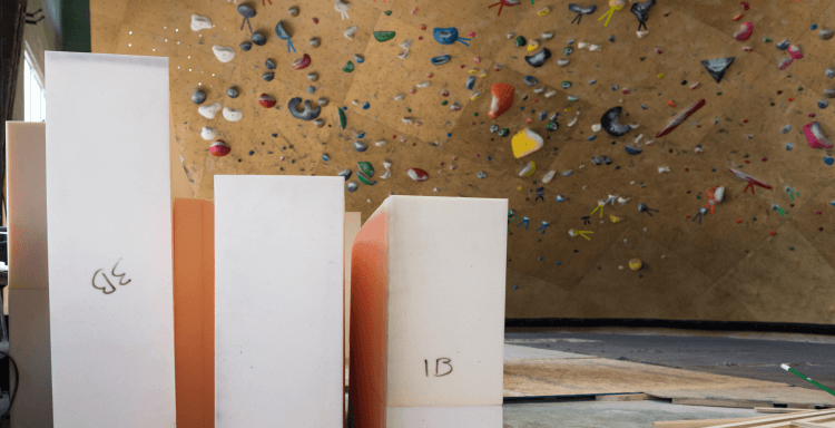 Bouldering pad foam blocks waiting for installation in front of a climbing wall