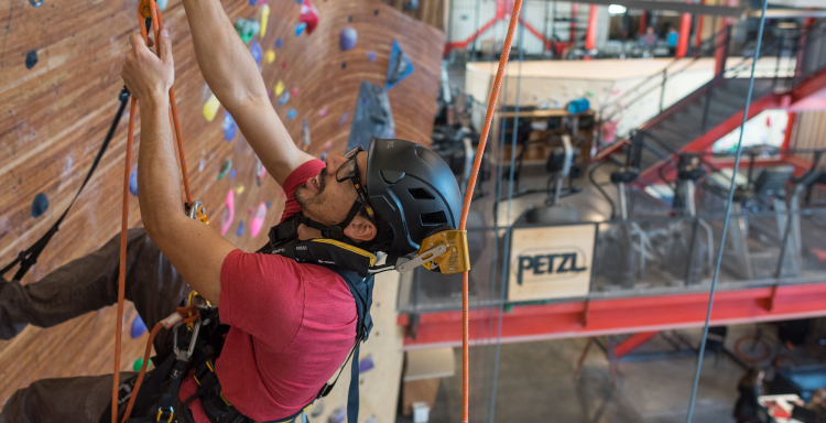 A route setter in Petzl safety gear ascending a climbing wall