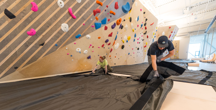 A man and woman installing a bouldering floor cover