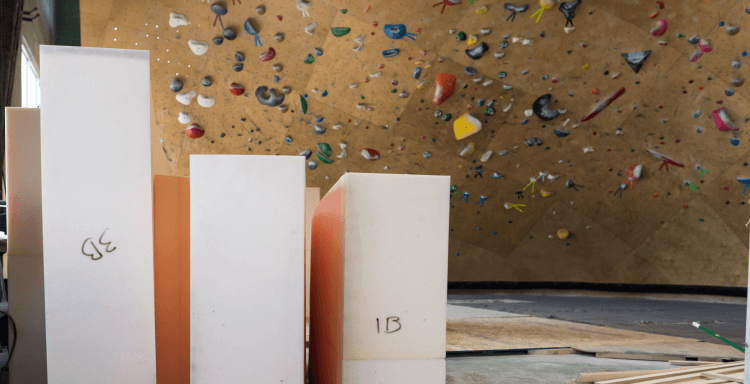 Bouldering pad foam blocks waiting for installation in front of a climbing wall