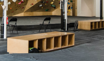 Wood storage benches and black folding chairs in a climbing gym