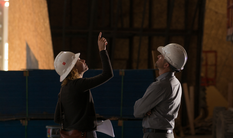 Two architects in hardhats point up at a climbing wall under construction