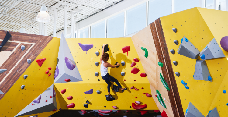 Woman bouldering on a stylish yellow and wood inlay climbing wall