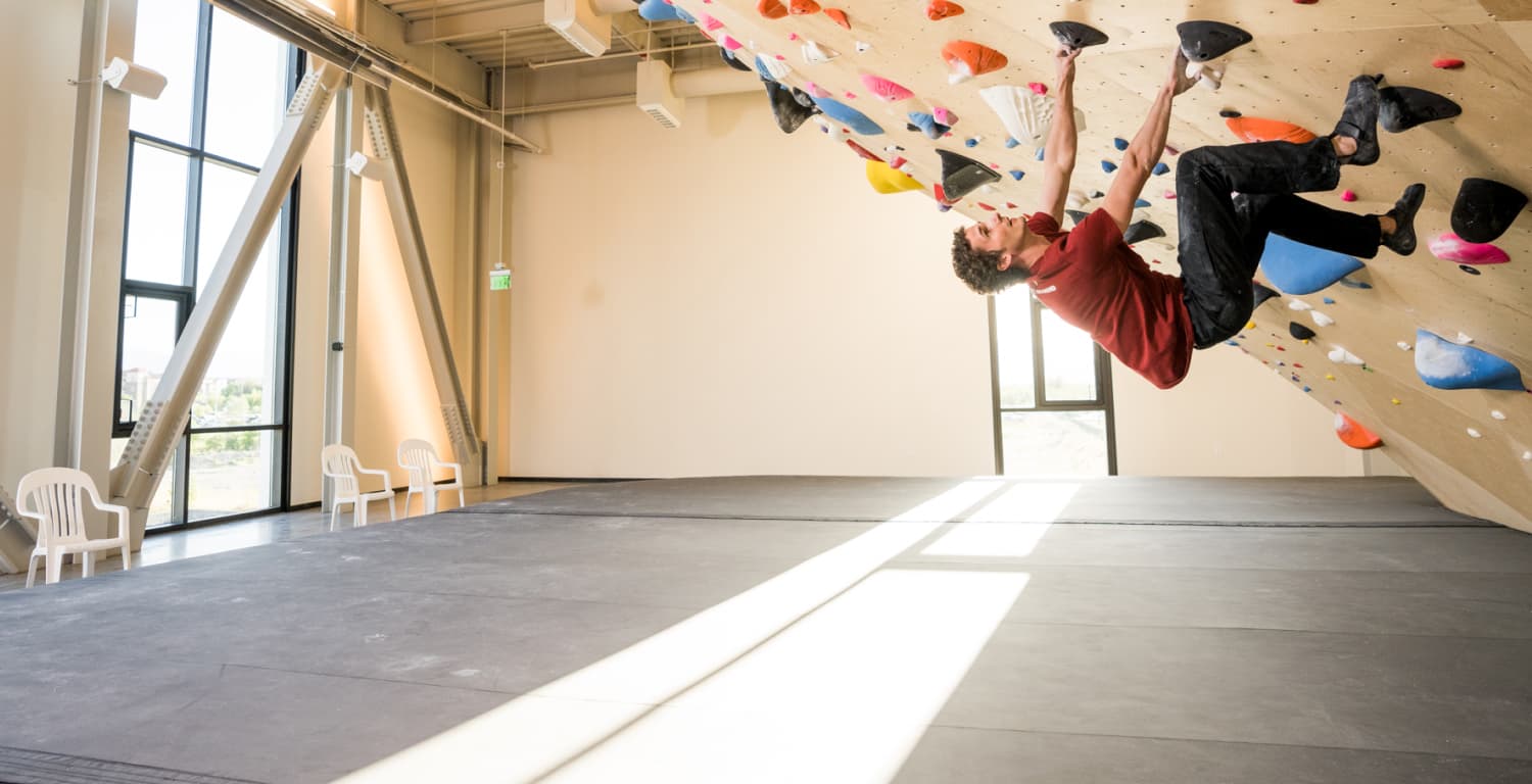 Man climbing an overhanging indoor bouldering wall in sunlight