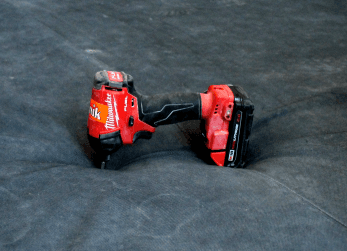 A red drill falls onto a nylon-covered bouldering pad