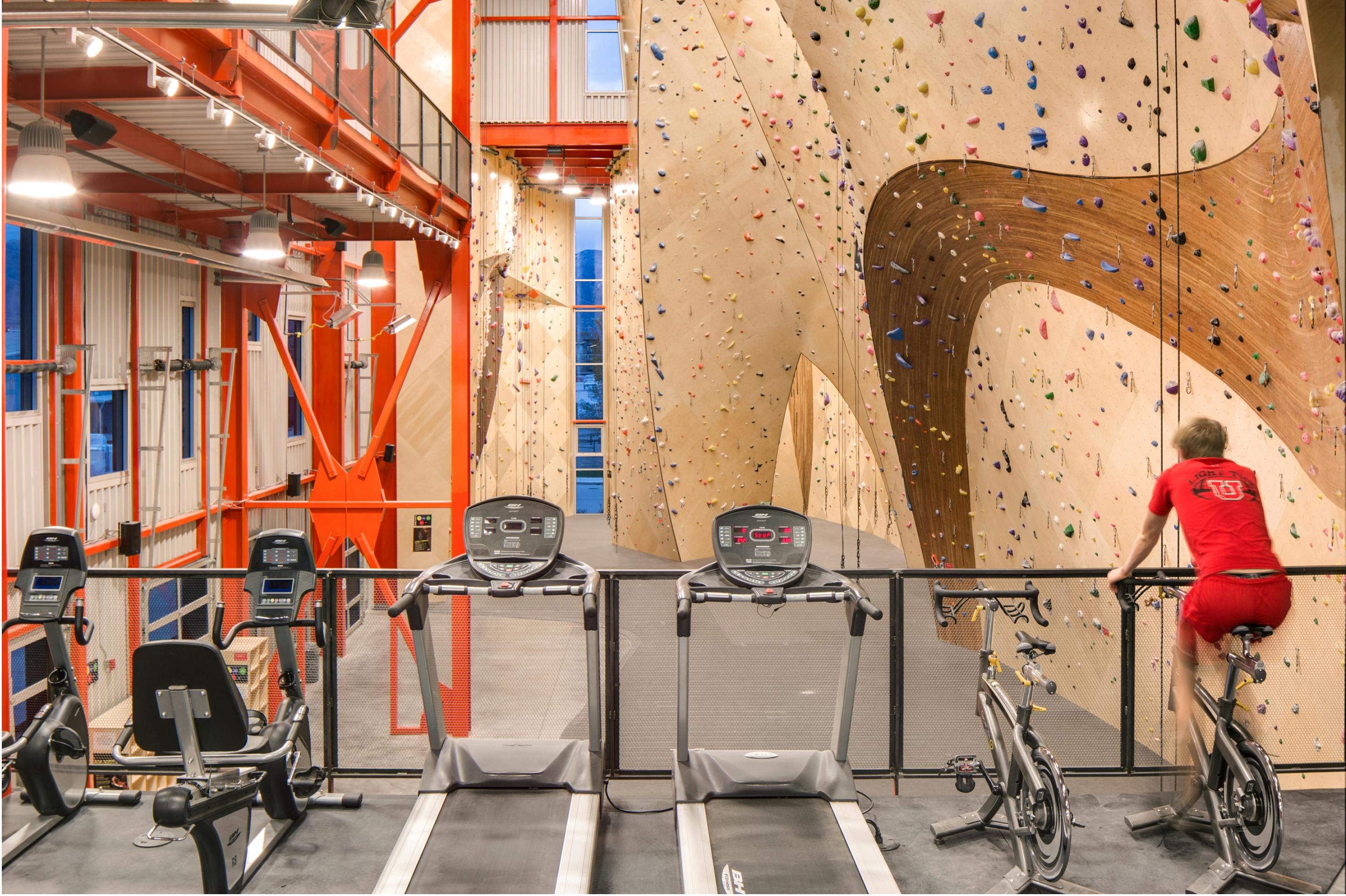 A man on a spin bike overlooks an indoor climbing gym