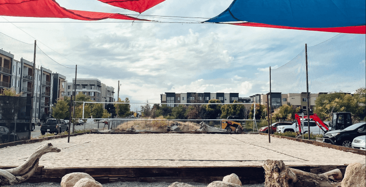 An urban sand volleyball court surrounded by trees and apartment buildings