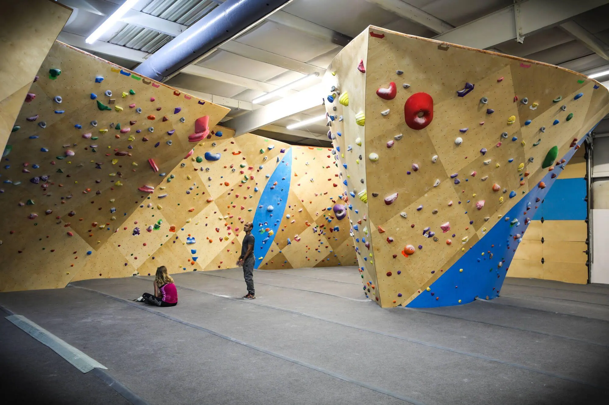 A classic view of the most challenging climbing walls in this gym. Two climbers are sizing up problems on The Wave, which have some intimidating heights.
