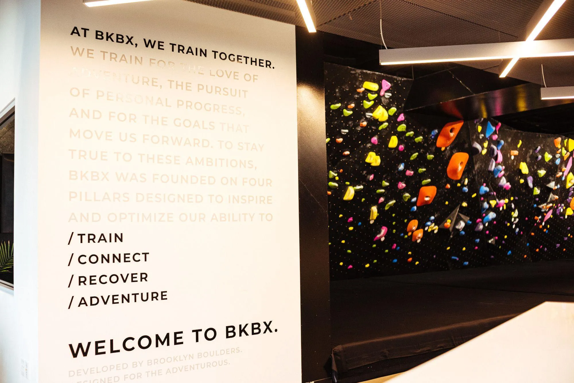 A view of the ARC walls next to BKBX's brand messaging - "At BKBX, we train together. We train for the love of adventure, the pursuit of personal progress, and for the goals that move us forward. To stay true to these ambitions, BKBX was founded on four pillars designed to inspire and optimize our ability to: train, connect, recover, and adventure."