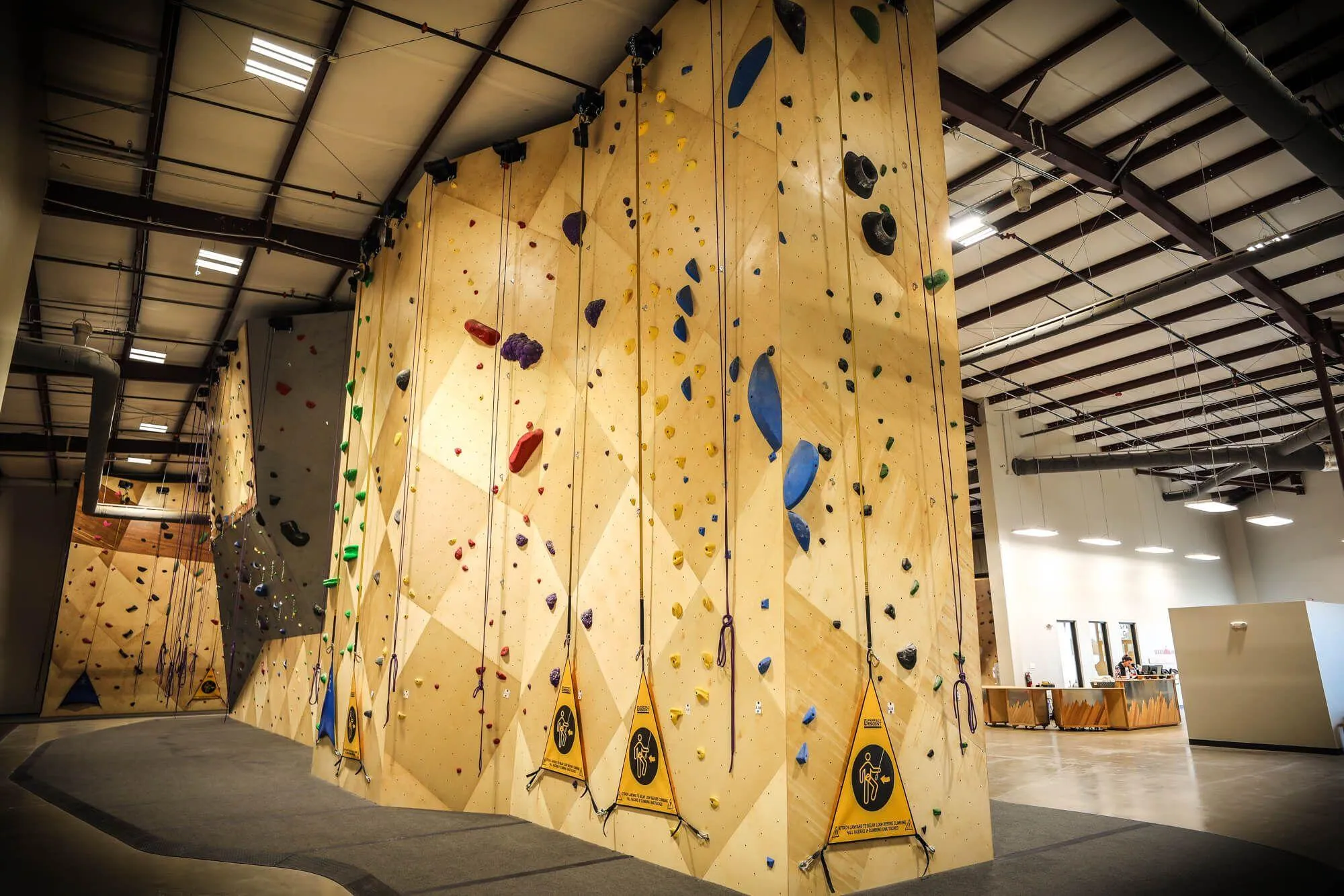 Another wide angle shot from one of the building corners. In the foreground is the backside of the standalone route climbing area with 5 auto-belays in-sight; the lengthy route climbing wall in the left background; the main entrance and custom front desk on the right.