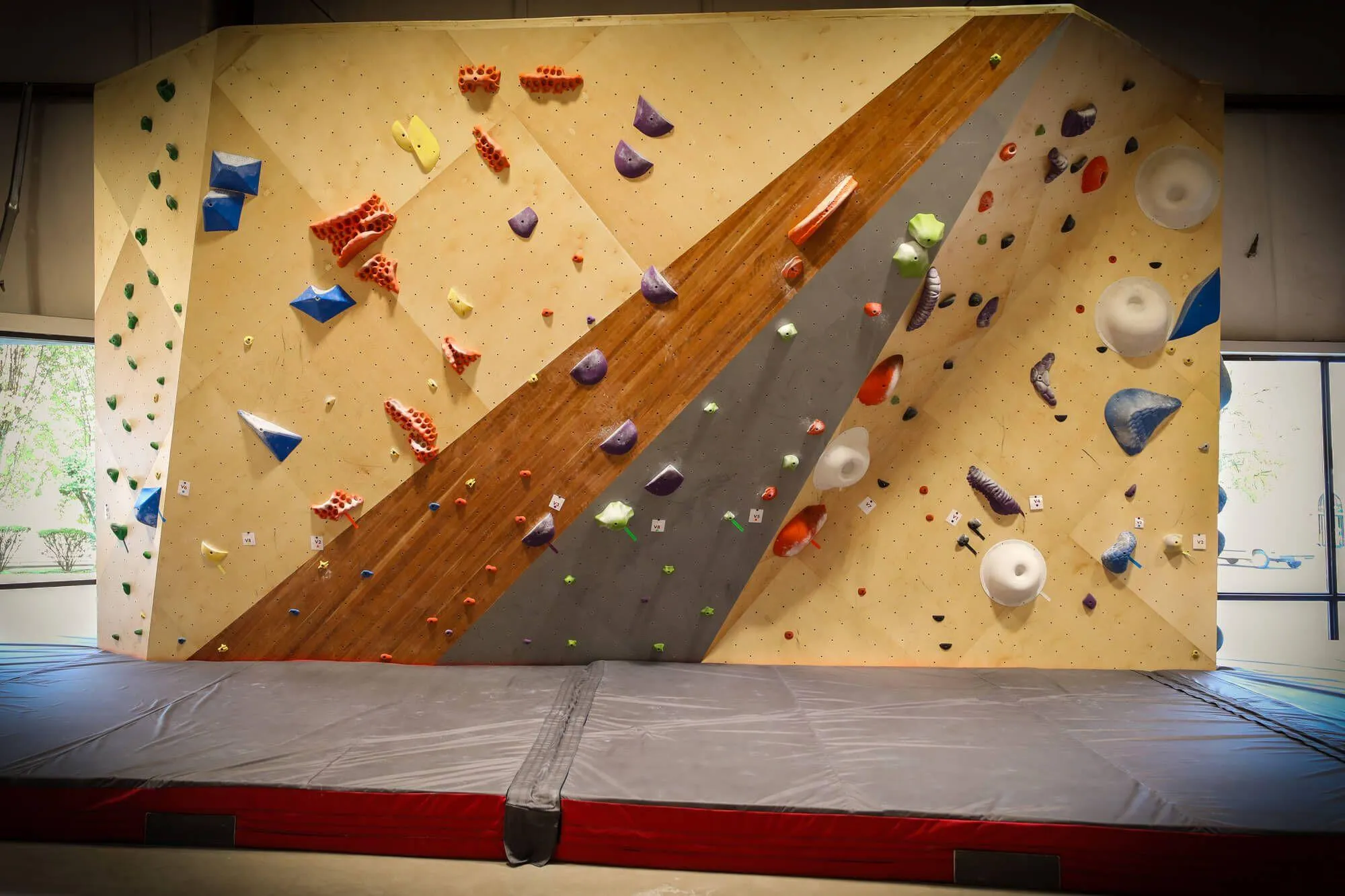 This climbing gym makes excellent use of all the space given to them by the building, as seen here with this short but stout bouldering wall between two windows letting natural light in. The wall was brought out to be significantly overhung in areas to create more challenging problems, while also incorporating the same branded hardwood and painted features of the rest of the gym.